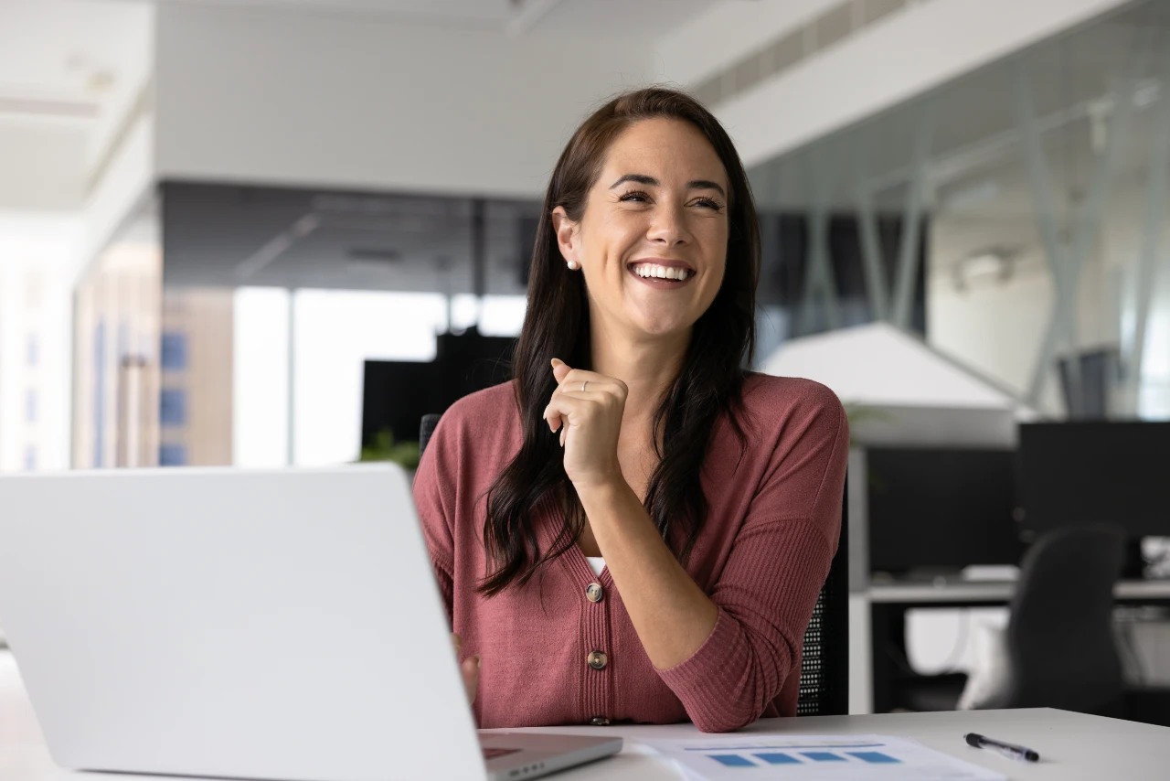 A smiling professional woman working at a laptop in a bright, modern office, representing the collaborative team at Step3 Digital